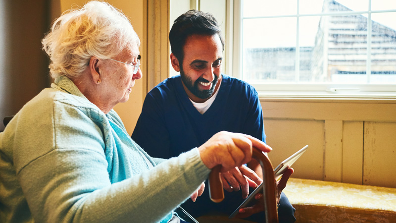 Un hombre de mediana edad está enseñando algo en una tablet a una una mujer de edad avanzada.