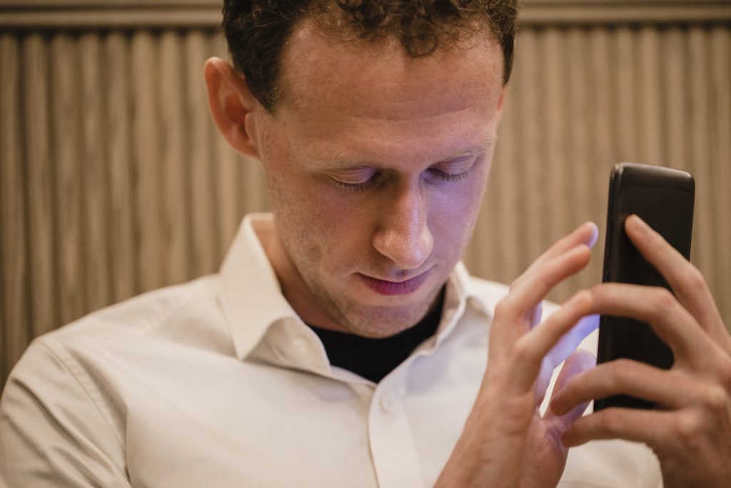 Um grande plano de um homem em roupa casual, segurando o seu smartphone na mão e utilizando uma aplicação móvel para deficientes visuais para o ajudar.