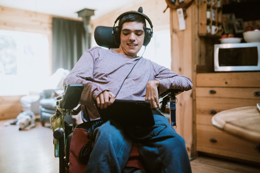 Una persona con disabilità seduta su una sedia a rotelle ha indosso delle cuffie ed sta utilizzando un tablet.