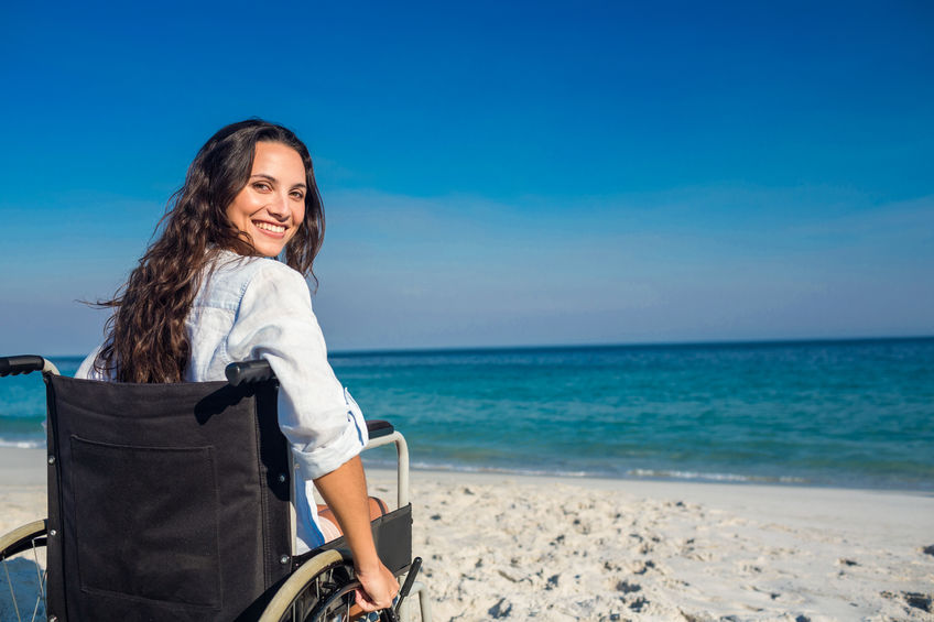 woman in wheelchair smiles at camera on beach in front of the sea