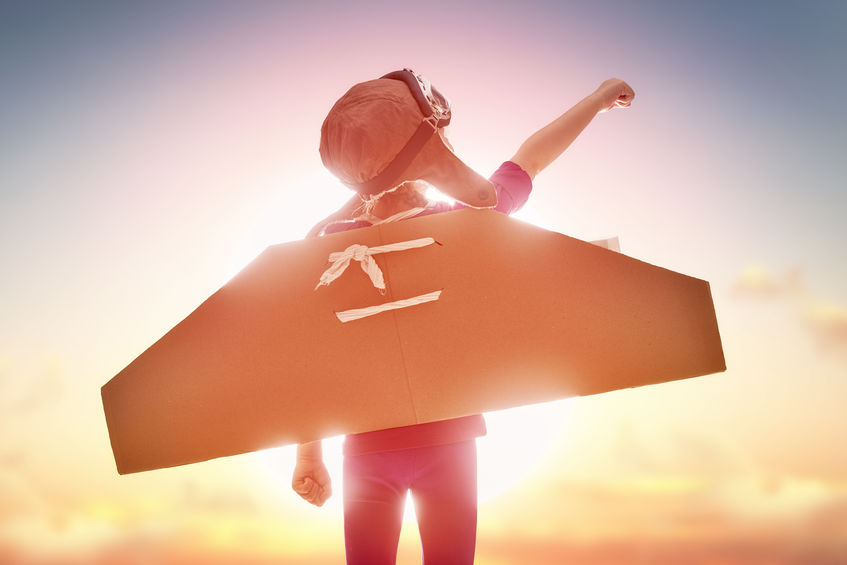 boy with cardboard airplane wings and a homemade aviator's helmet points to the sky