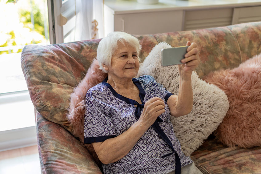 elderly woman using a smartphone while sitting on a sofa