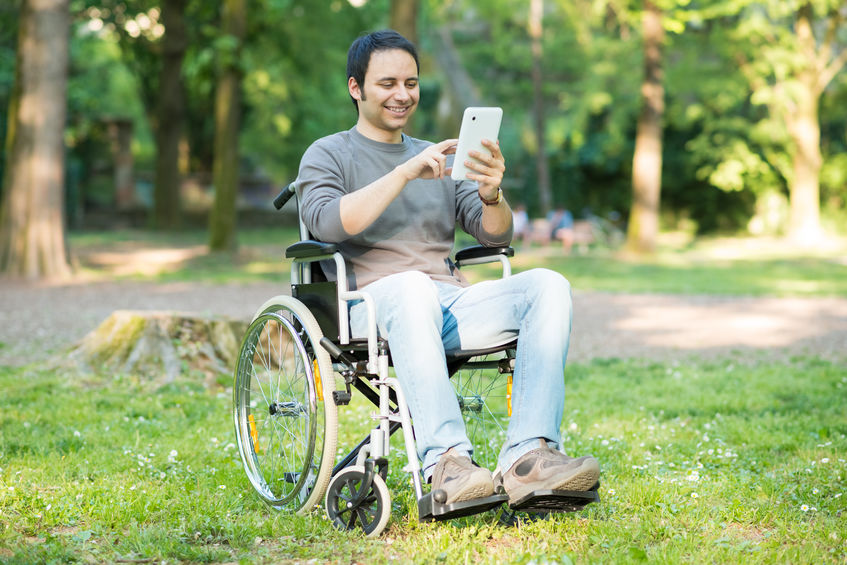 Hombre utilizando una silla de ruedas en un parque que interactúa con una tableta digital
