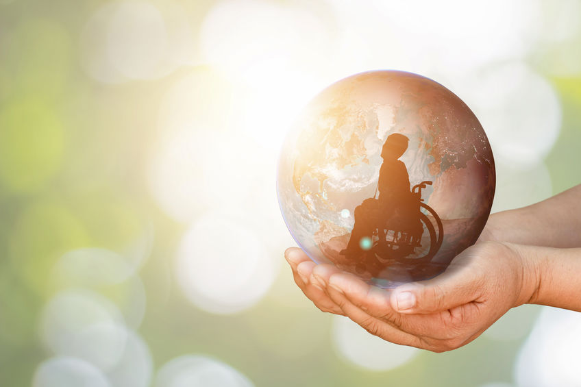 hands hold a ball of the world with a person sitting in a wheelchair inside it
