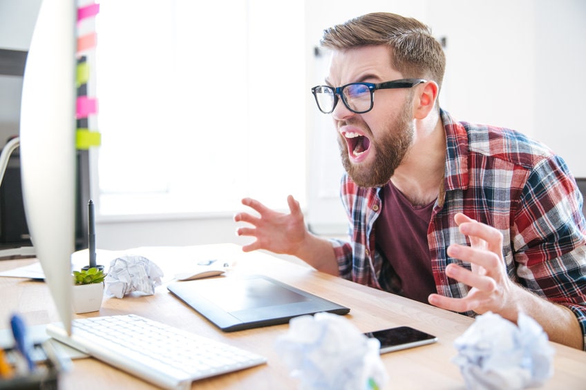 Hombre con barba enfadado y gritando mirando el monitor del ordenador