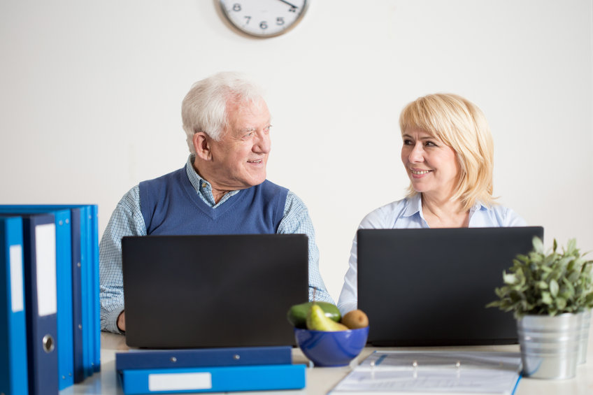 Pareja de ancianos empresarios se miran sonriendo delante del ordenador mientras navegan utilizando accesibilidad web