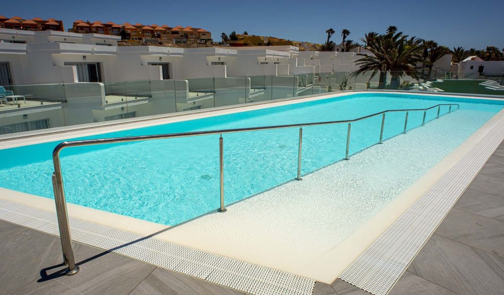 piscina exterior com uma rampa muito longa com corrimão adaptado para pessoas deficientes, rodeada pelos edifícios e quartos do hotel.
