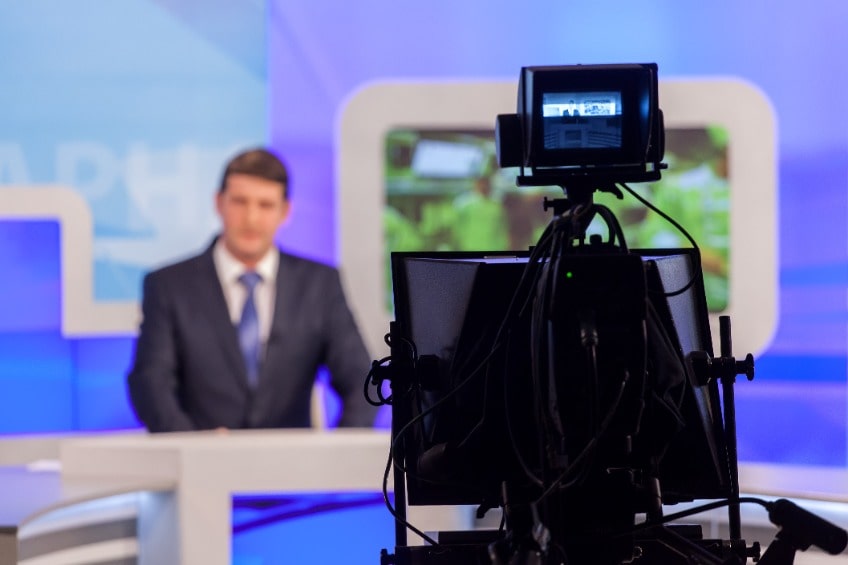Presentador de informativos de televisión siendo grabado en directo por una cámara
