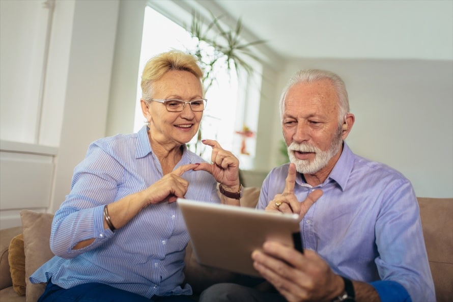 Una pareja de personas mayores utilizan una tablet mientras hablan en lengua de signos.