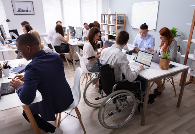 Equipo de desarrolladores trabajando en una oficina, entre ellos vemos a un empleado en silla de ruedas.